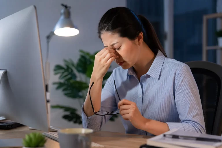 Een vrouw neemt pauze van haar computerwerk en wrijft vermoeid in haar ogen.