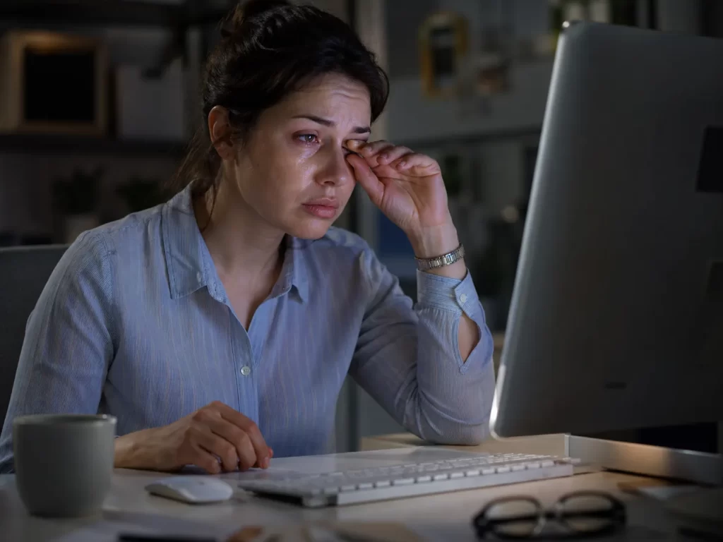 Een vermoeide vrouw wrijft in haar tranende ogen tijdens langdurig computergebruik.