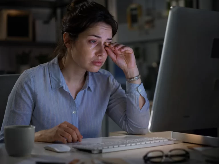 Een vermoeide vrouw wrijft in haar tranende ogen tijdens langdurig computergebruik.